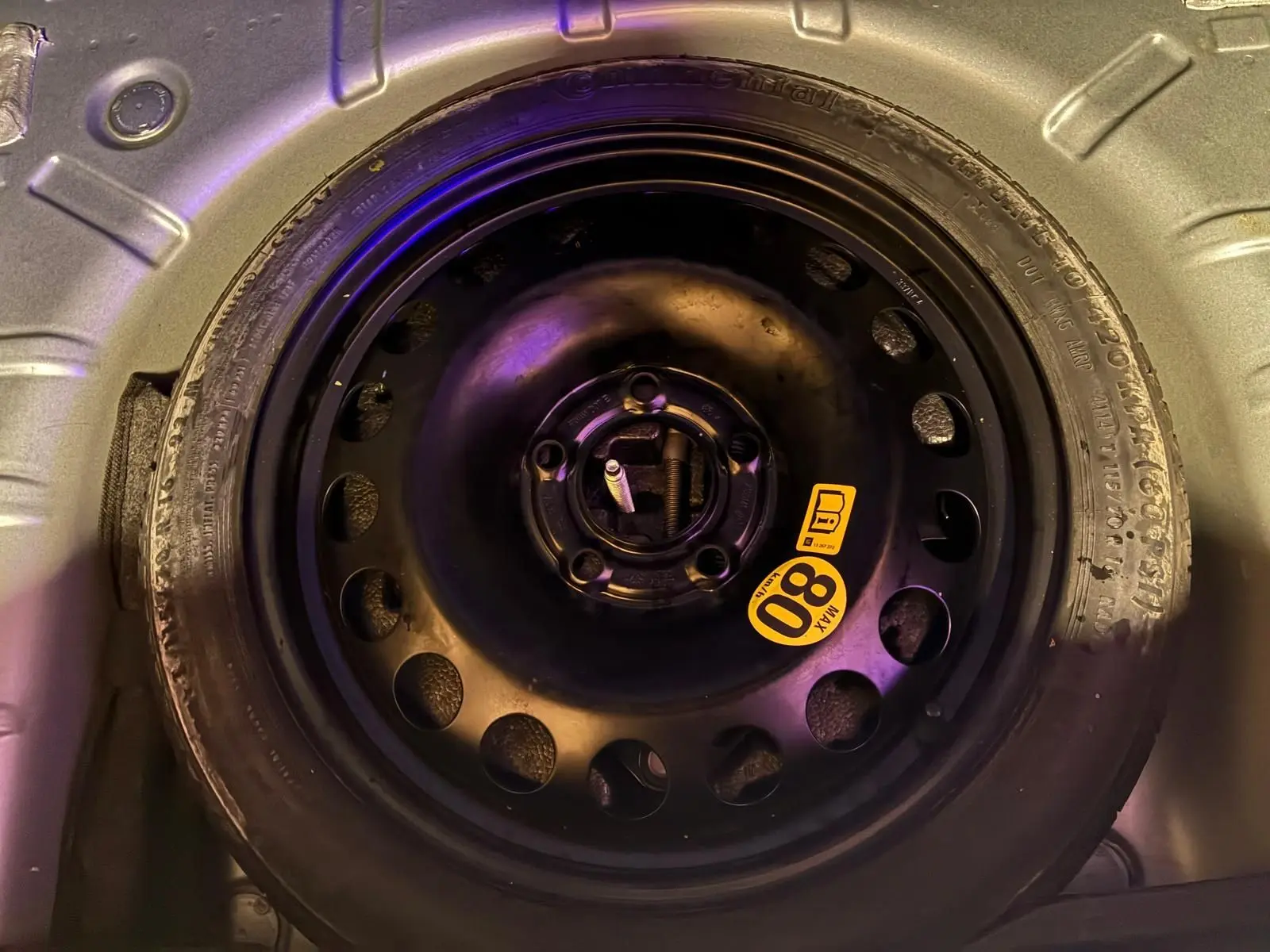 Gros plan sur la roue de secours noire avec étiquette jaune 80 km/h dans le coffre d'une Opel Astra gris 2015.
