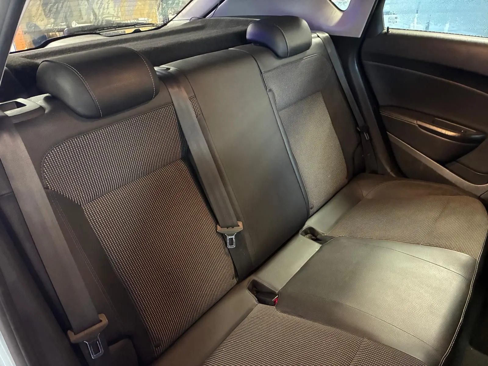 Vue intérieure de la banquette arrière en tissu et cuir noir de l’Opel Astra 1.6 CDTI gris, avec ceintures de sécurité visibles.