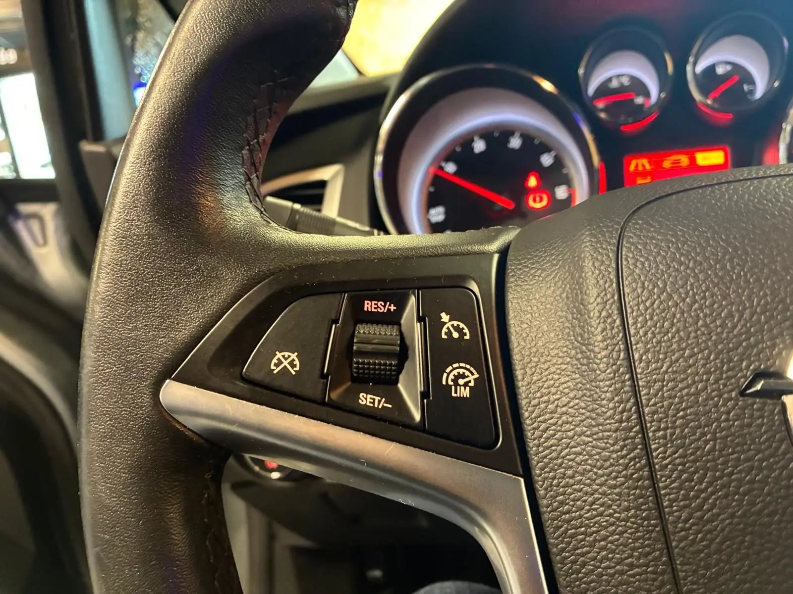 Gros plan sur le volant noir de l’Opel Astra 2015 avec commandes de régulateur de vitesse et tableau de bord éclairé.