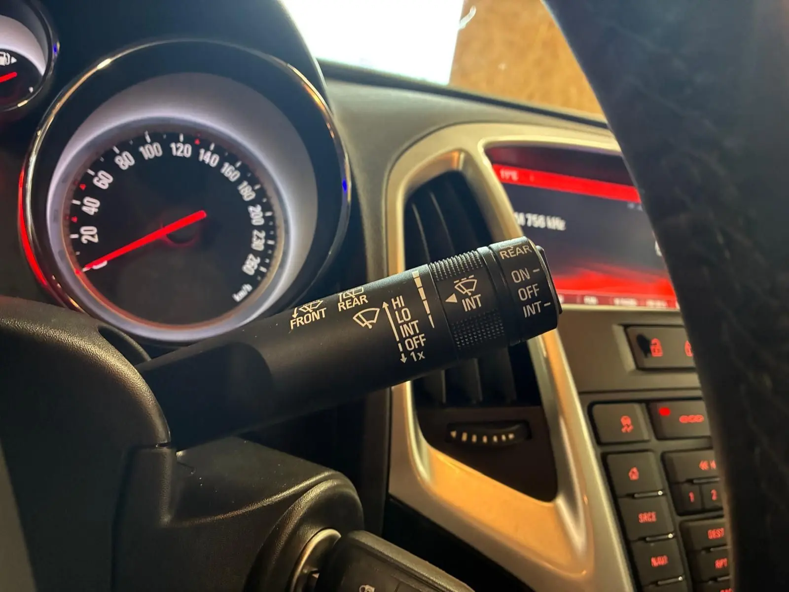 Gros plan sur le commodo d’essuie-glace à gauche du volant dans l’habitacle gris d’une Opel Astra 2015.