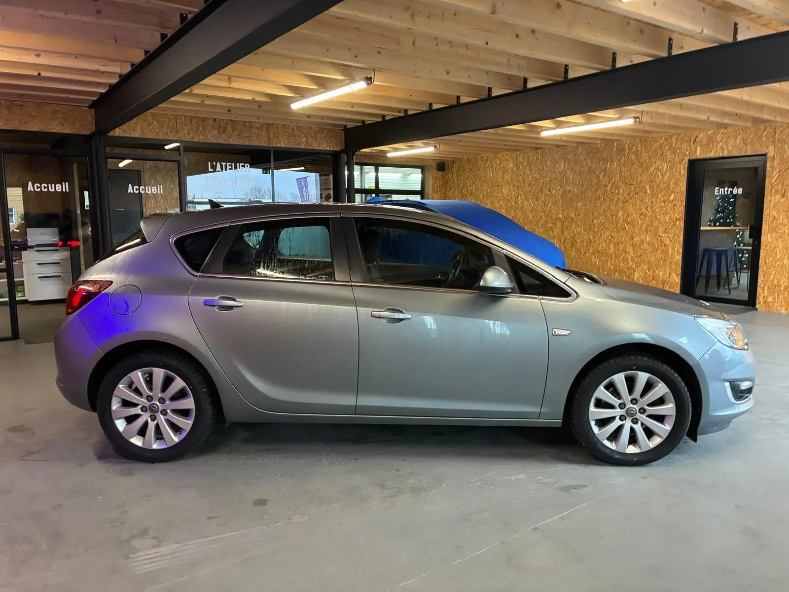 Vue de profil côté gauche d'une Opel Astra gris métallisé de 2015 stationnée dans un garage avec murs en bois.