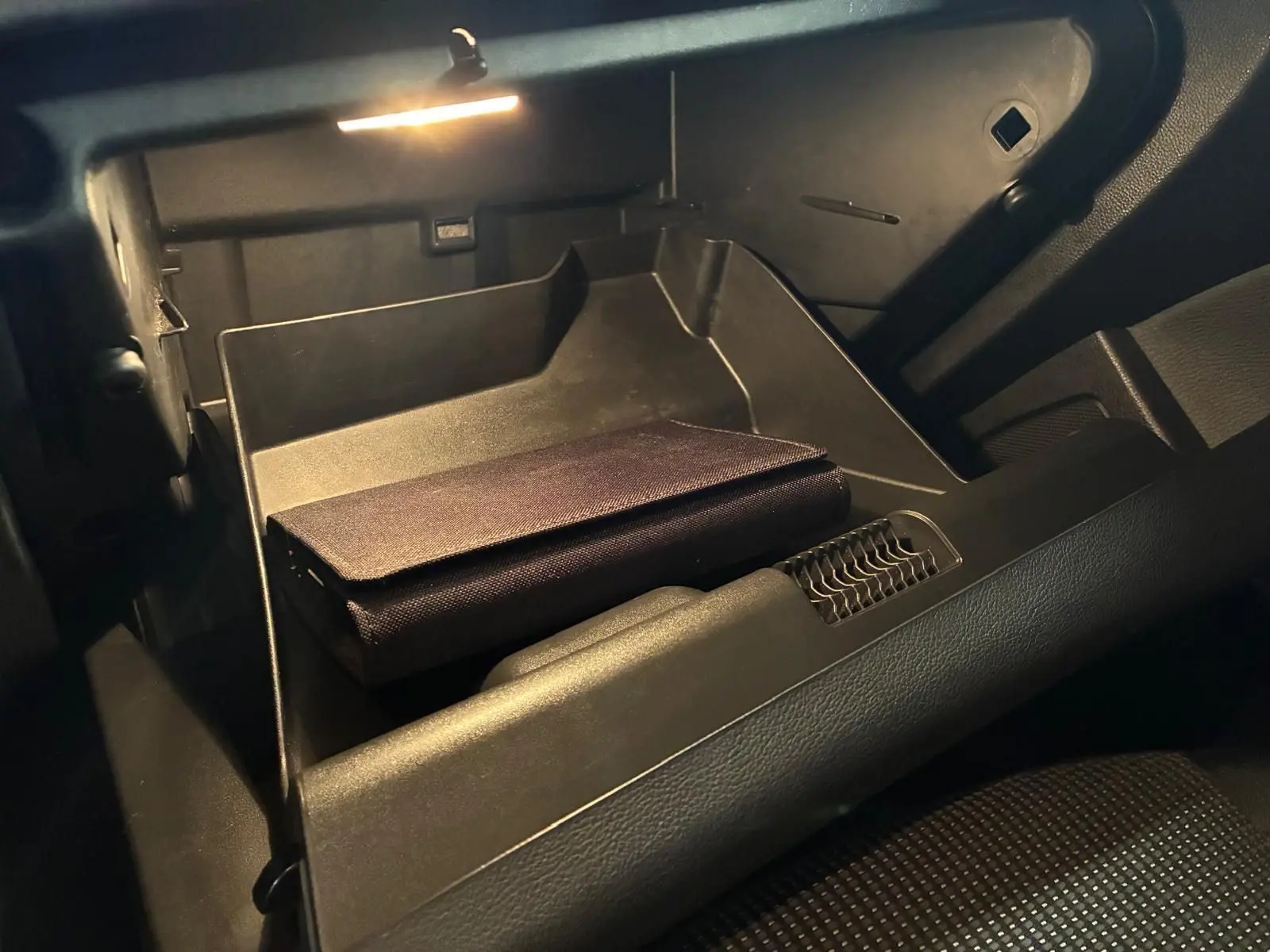Vue intérieure du vide-poche passager éclairé d'une Opel Astra gris 2015, avec un étui noir posé à l'intérieur.