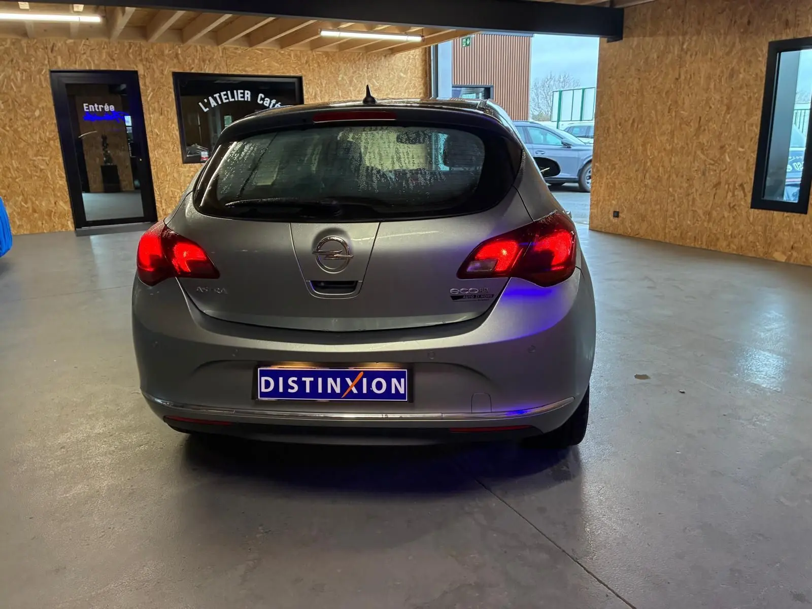 Vue arrière d'une Opel Astra gris métallisé de 2015 avec feux allumés dans un garage intérieur.