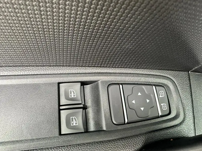 Gros plan sur les commandes de lève-vitres et réglage des rétroviseurs côté conducteur du Nissan Townstar gris 2024.