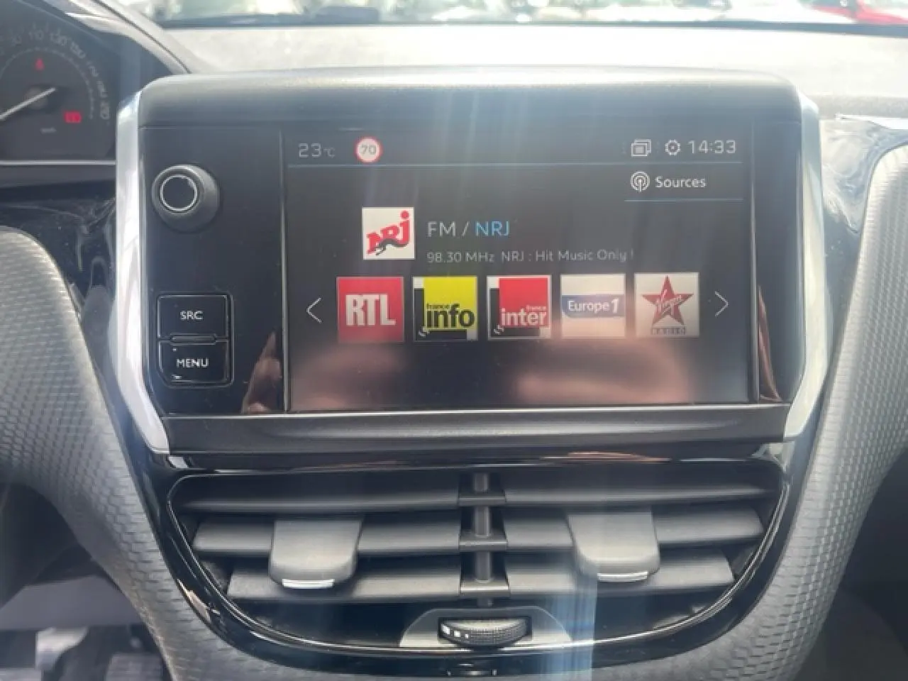 Écran tactile central de la Peugeot 208 blanc perle, affichant les stations radio FM avec commandes autour.