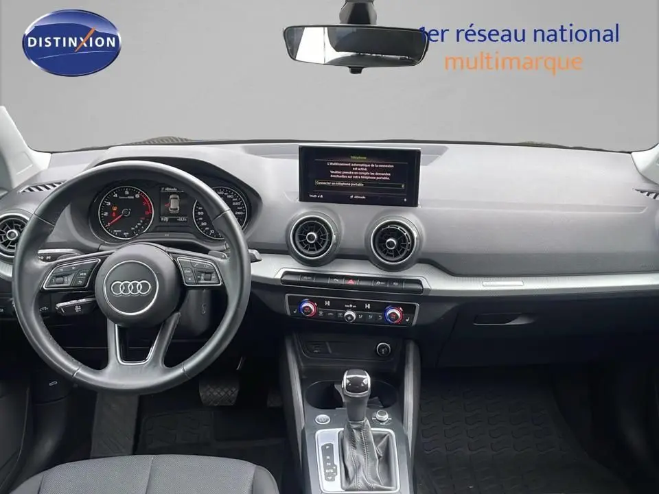Intérieur de l'Audi Q2 35 TFSI S-Line 2023, vue frontale du tableau de bord avec volant multifonction et écran central.