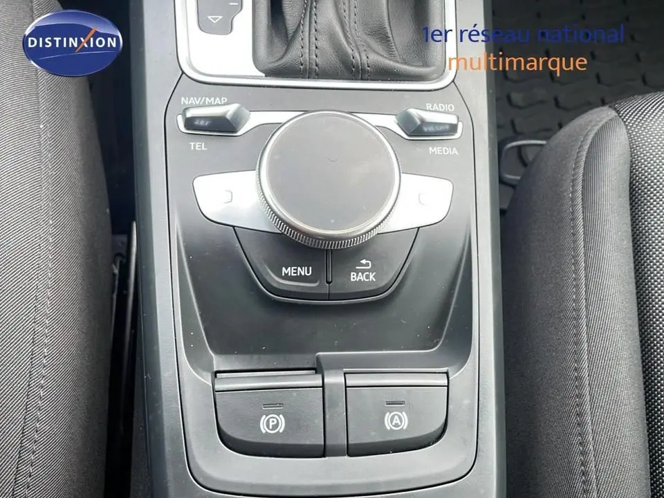 Gros plan sur la console centrale noire de l'Audi Q2 35 TFSI S-Line 2023, avec molette de contrôle et boutons de stationnement.