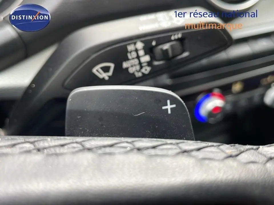 Gros plan sur la palette de changement de vitesse "+" du volant d'un Audi Q2 35 TFSI S-Line noir, avec commandes de climatisation en arrière-plan.