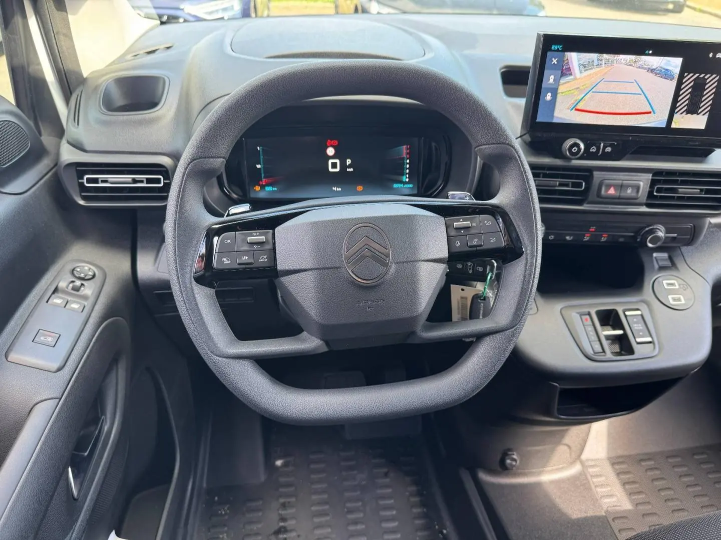 Vue intérieure centrée sur le volant multifonction et l'écran tactile affichant la caméra de recul du Citroën Berlingo XL blanc.