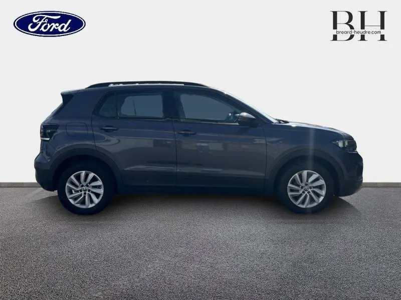 Profil côté gauche d'un Volkswagen T-Cross gris cendré métallisé, avec jantes alliage et vitres teintées.