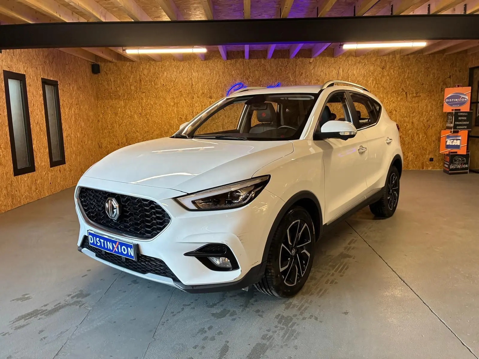 Vue 3/4 avant d’un MG ZS blanc 2022 dans un intérieur en bois, avec calandre noire et jantes noires distinctives.
