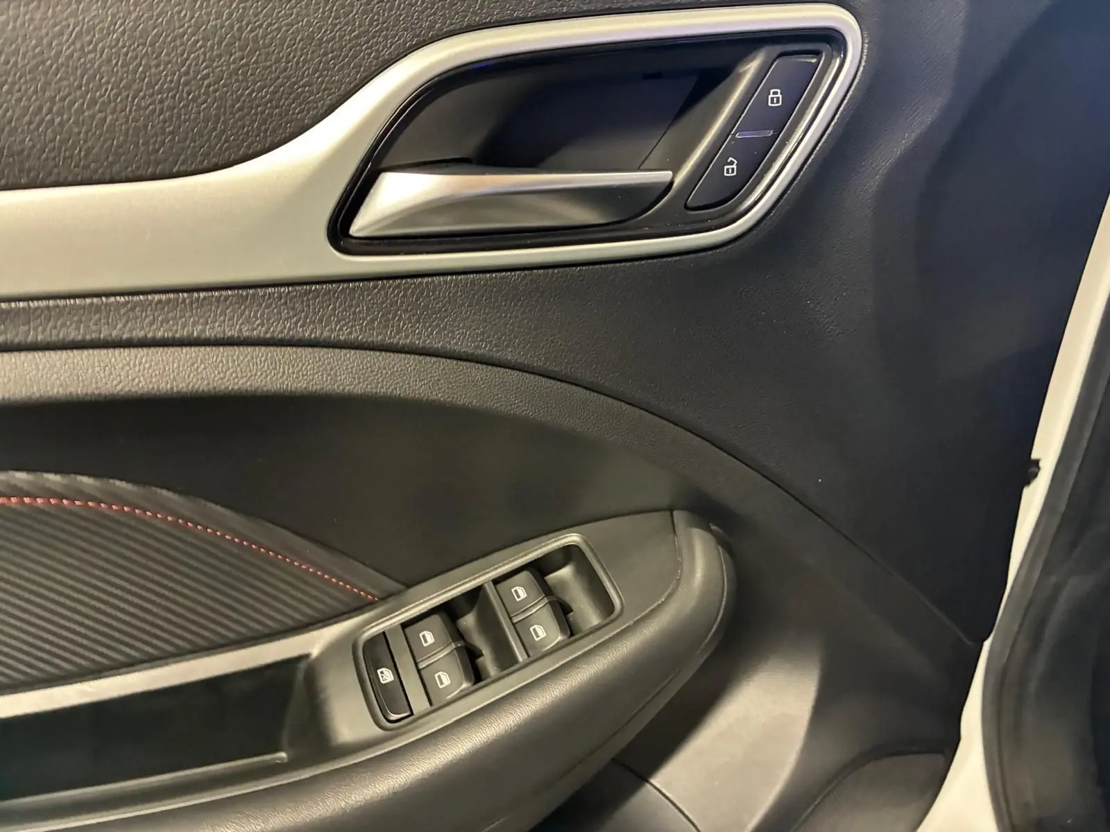 Gros plan sur la porte intérieure côté gauche du MG ZS blanc, avec commandes de vitres et verrouillage visibles.