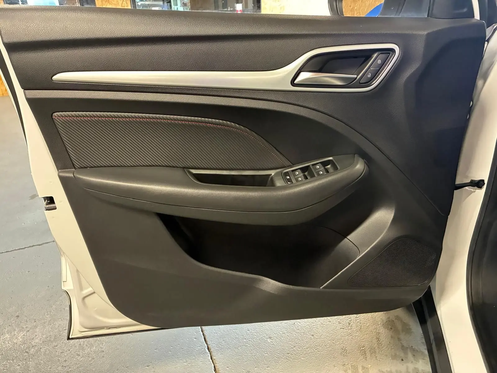 Vue de la porte avant gauche ouverte d’un MG ZS blanc 2022, intérieur noir avec commandes de vitres et poignée intégrée.