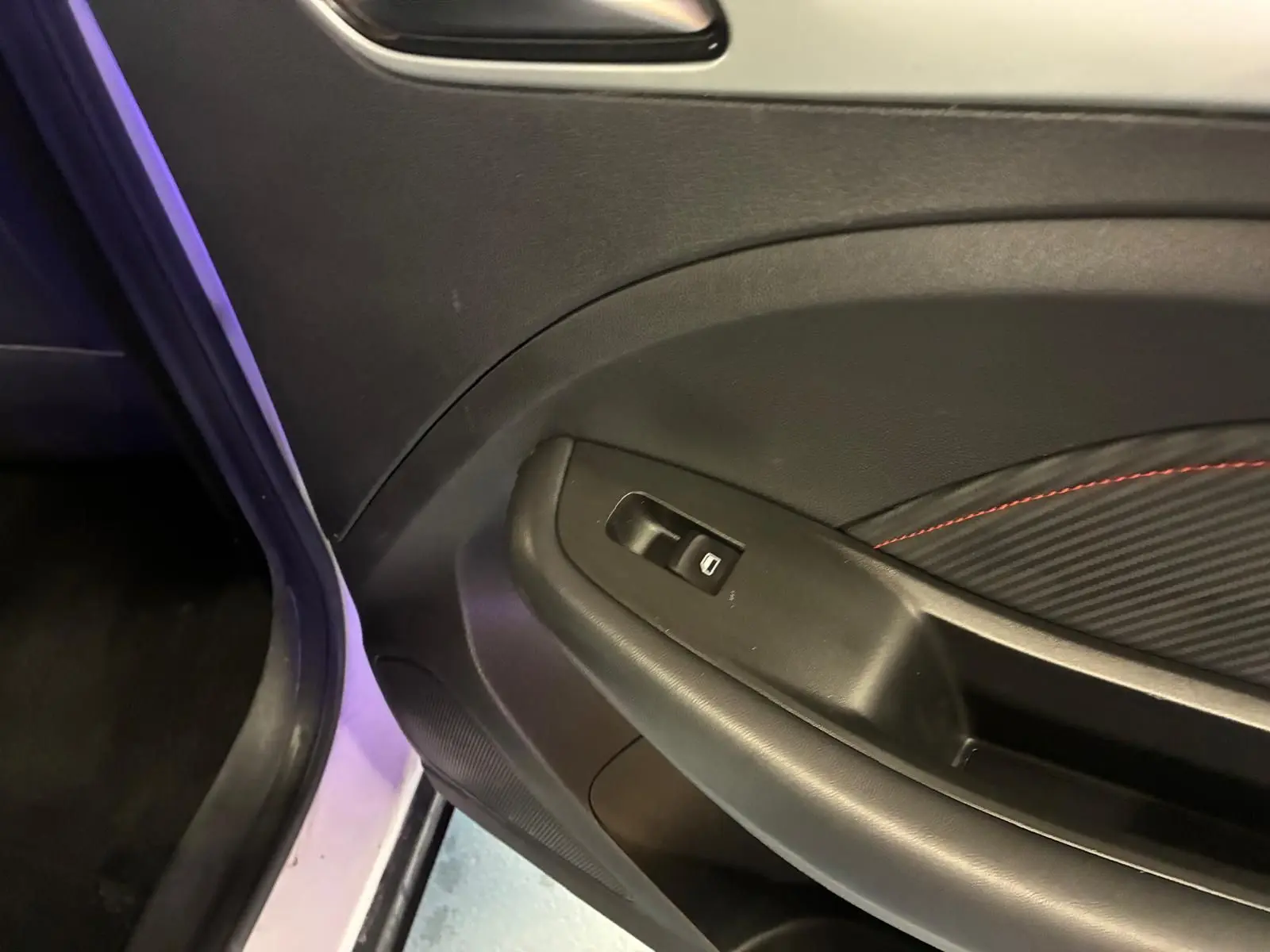 Gros plan sur la porte intérieure côté gauche d’un MG ZS blanc, avec garniture noire et surpiqûres rouges.