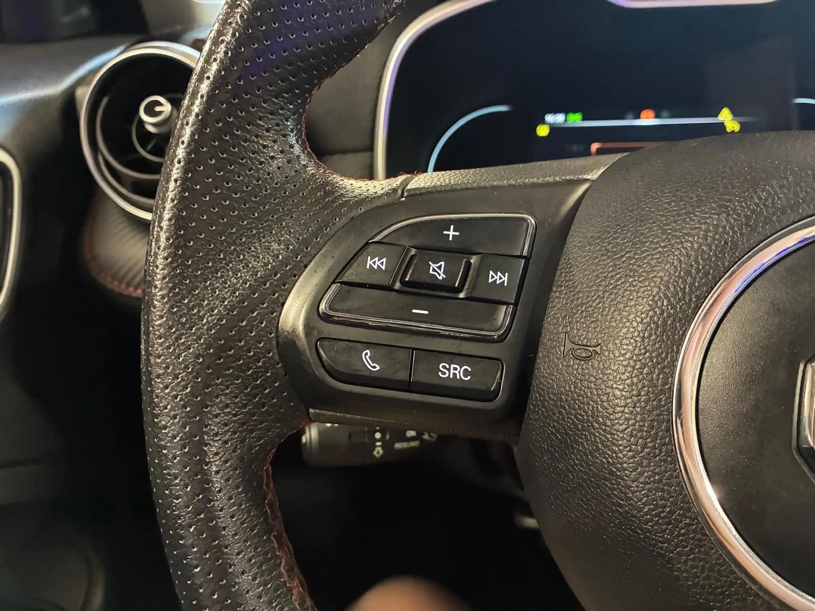 Gros plan sur le côté gauche du volant en cuir noir perforé du MG ZS blanc, avec commandes audio et téléphone intégrées.