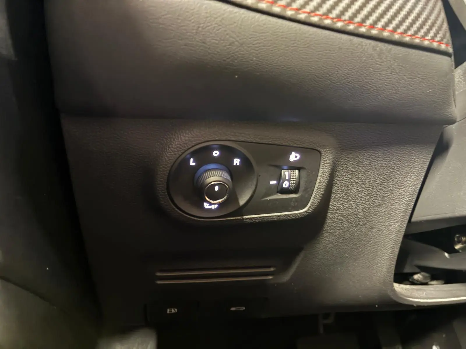 Gros plan sur les commandes de réglage des rétroviseurs et des phares du MG ZS blanc, intérieur noir.