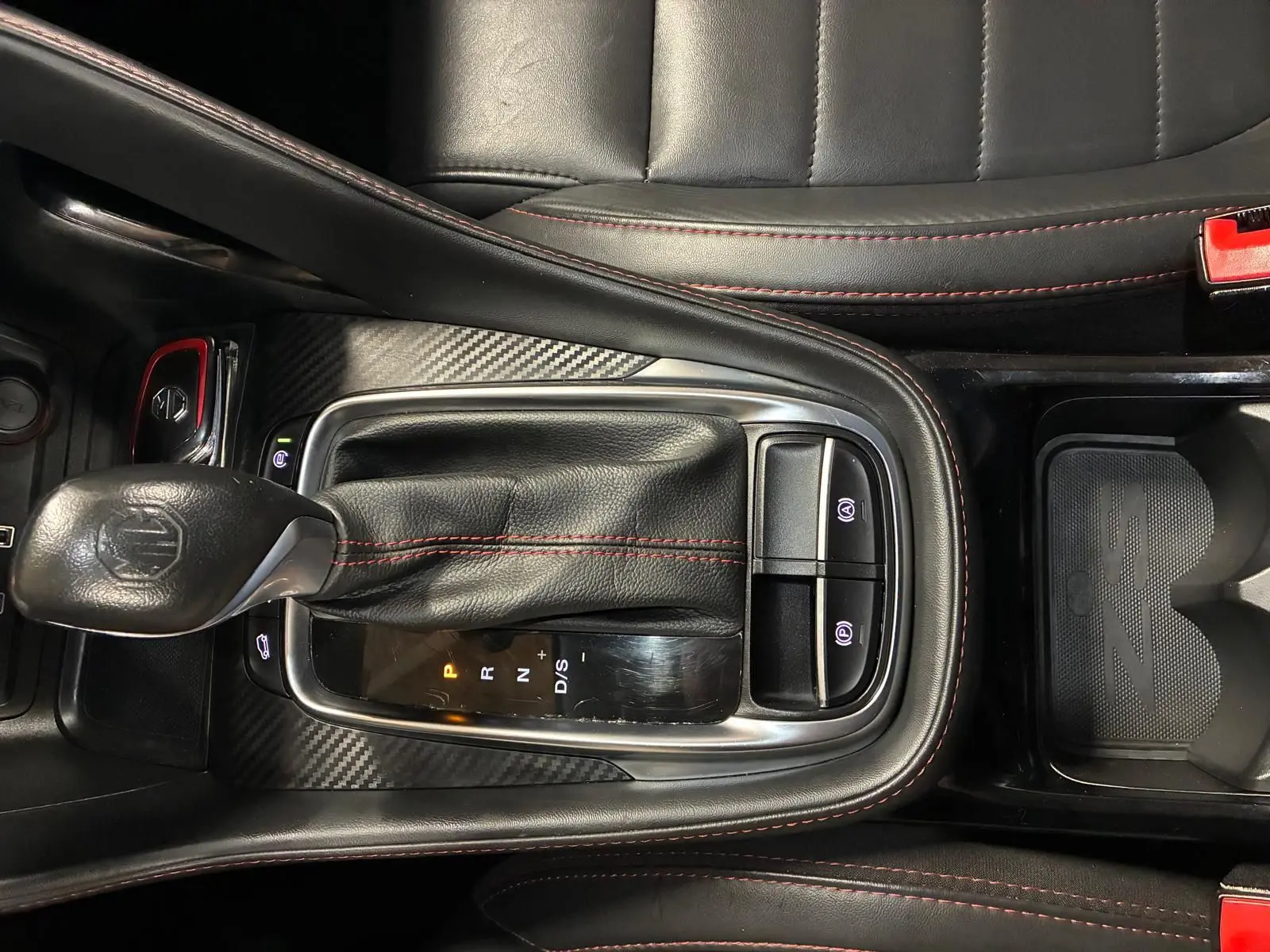 Vue rapprochée de la console centrale noire avec levier de vitesse cuir et surpiqûres rouges du MG ZS blanc 2022.