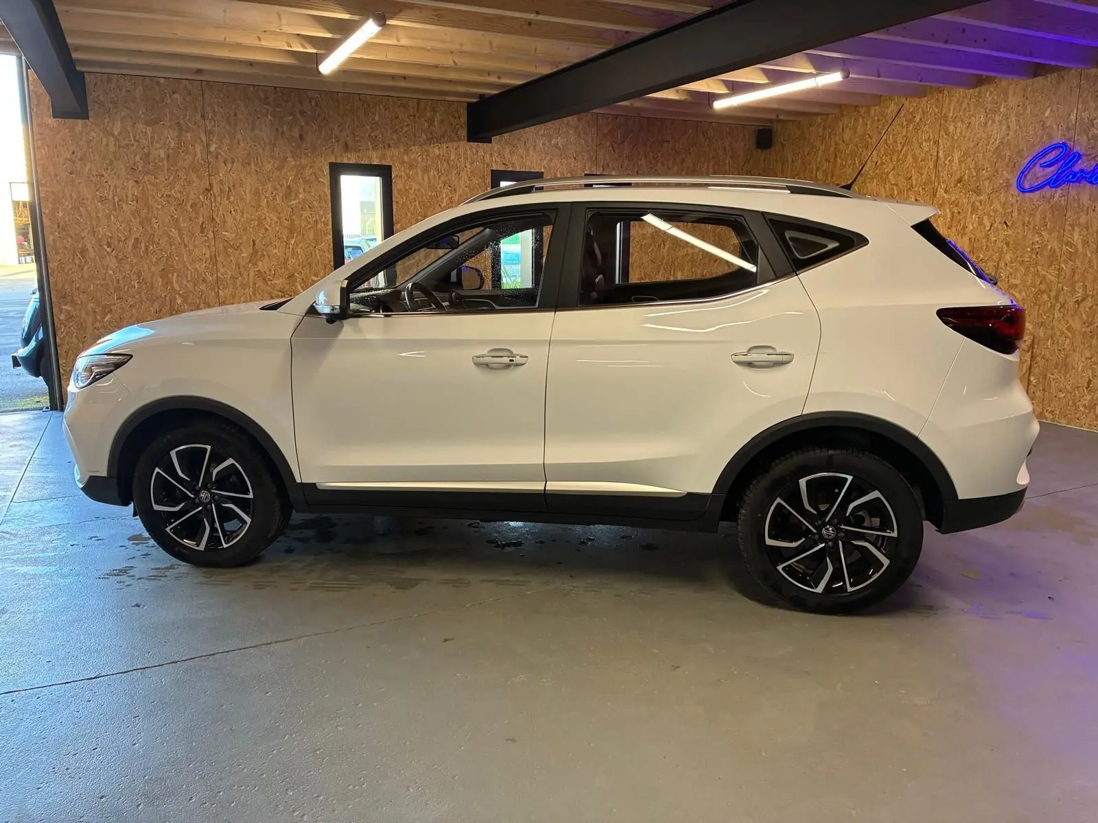 Vue de profil côté gauche d’un MG ZS blanc 2022 avec jantes alliage noires et toit ouvrant en intérieur bois.