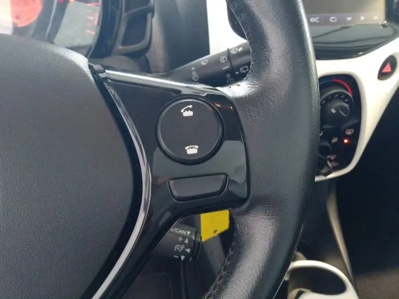 Gros plan sur les commandes téléphoniques du volant cuir noir d'une Citroën C1 blanche, avec tableau de bord partiel visible.