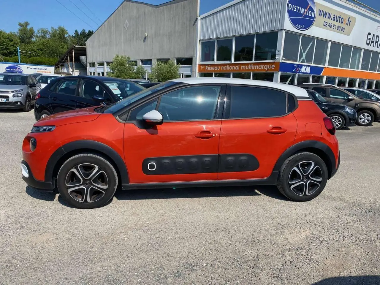 Profil côté gauche d'une Citroën C3 orange avec toit blanc et protections latérales noires en concession.