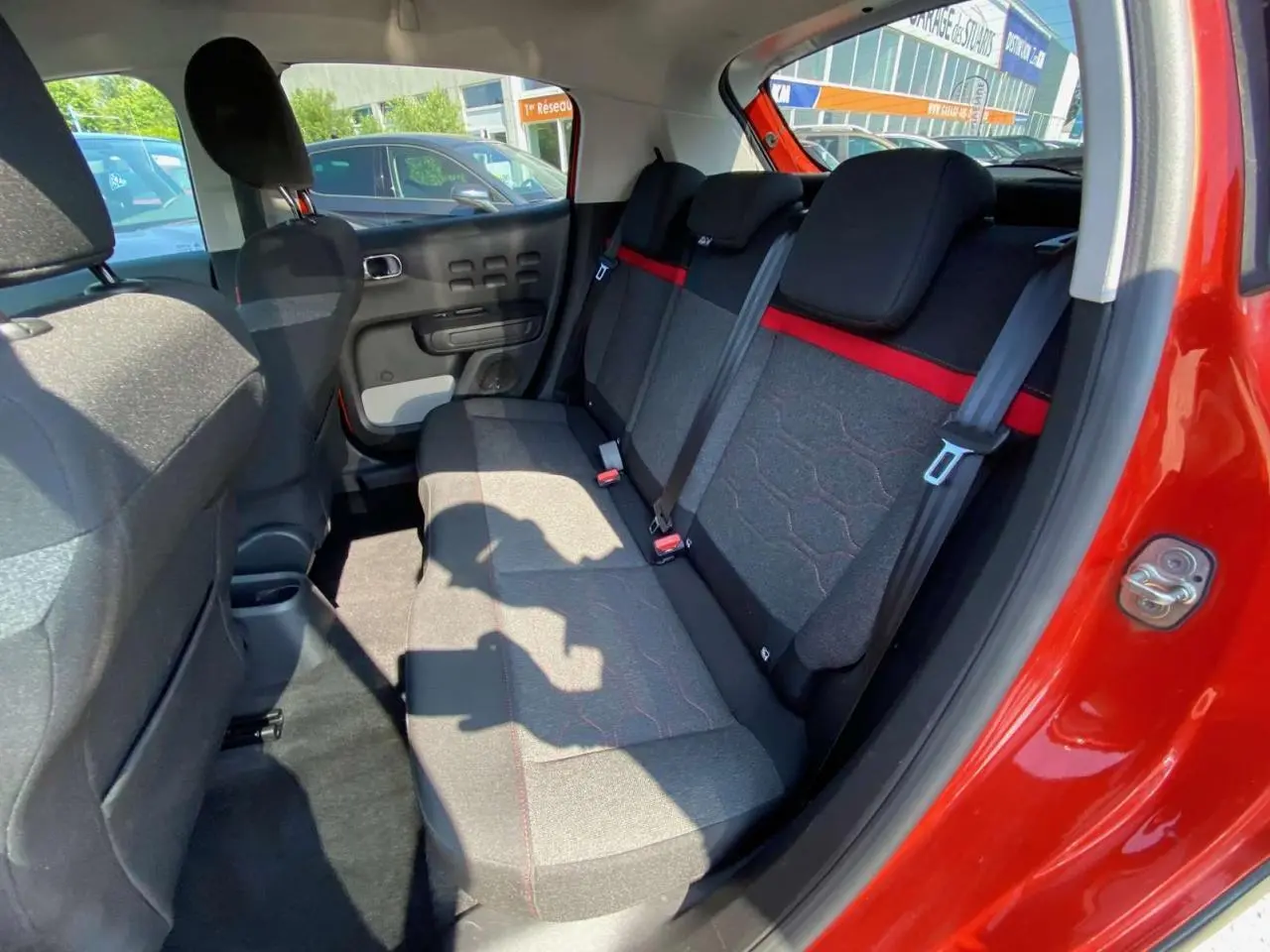 Intérieur arrière de la Citroën C3 orange 2018, banquette tissu gris avec bande rouge et ceintures de sécurité visibles.