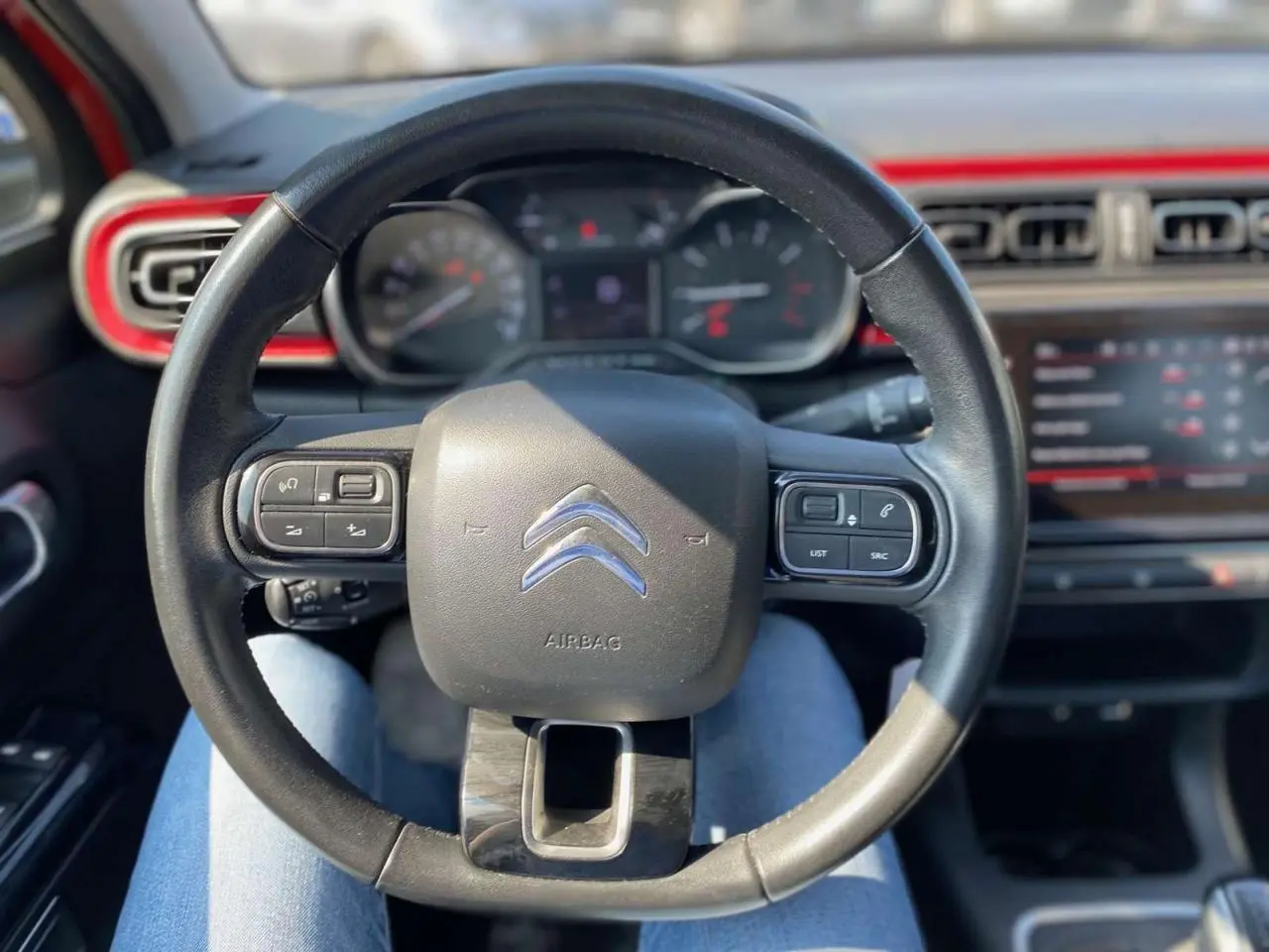 Vue rapprochée du volant noir de la Citroën C3 2018 avec tableau de bord et écran tactile rouge en arrière-plan.