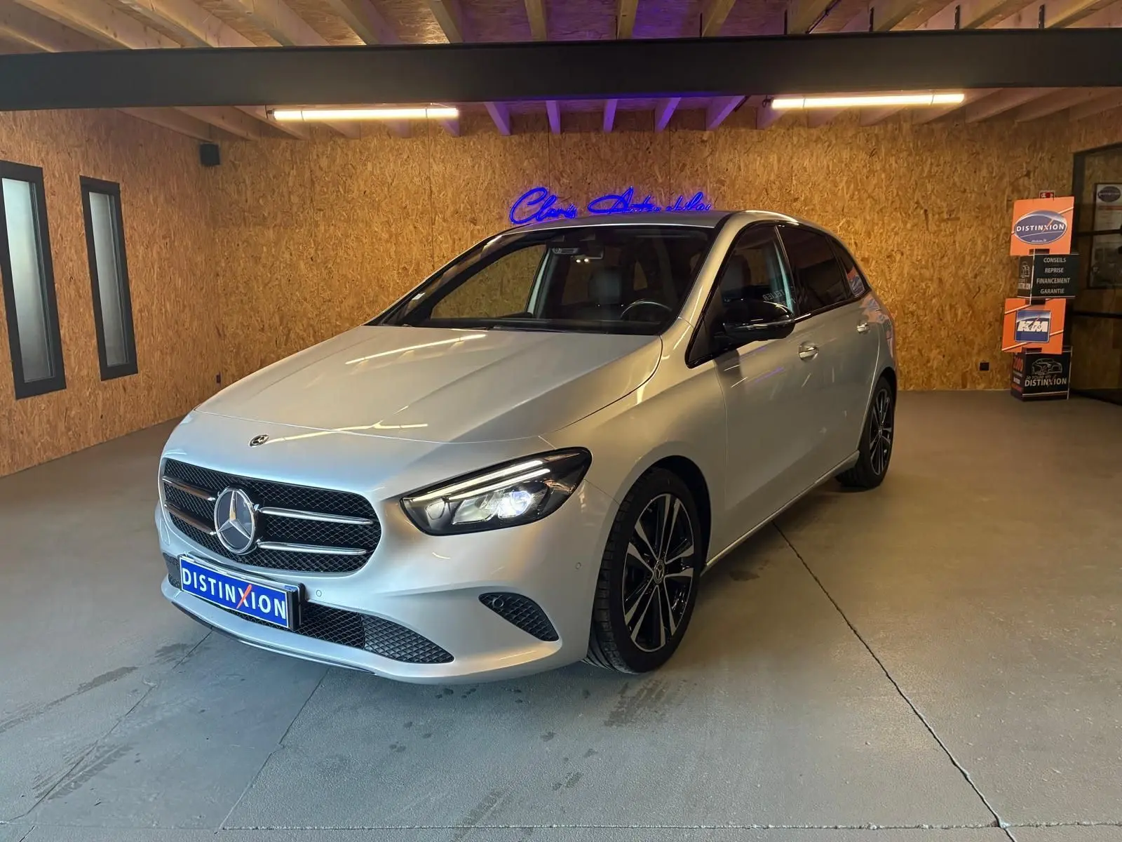 Vue 3/4 avant droite d'une Mercedes Classe B 200D Progressive Line gris métallisé avec jantes noires en intérieur showroom.