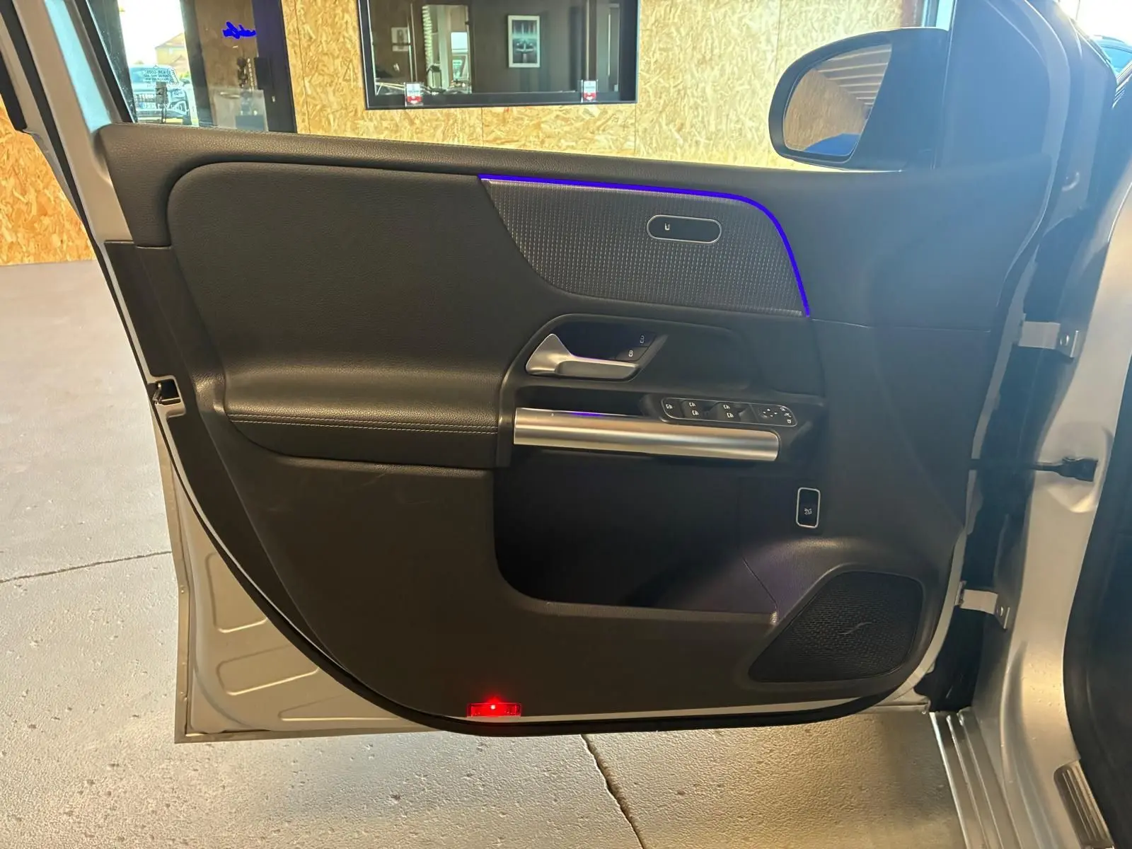 Vue intérieure de la porte avant gauche gris foncé d'une Mercedes Classe B 200D Progressive Line avec éclairage d'ambiance bleu.