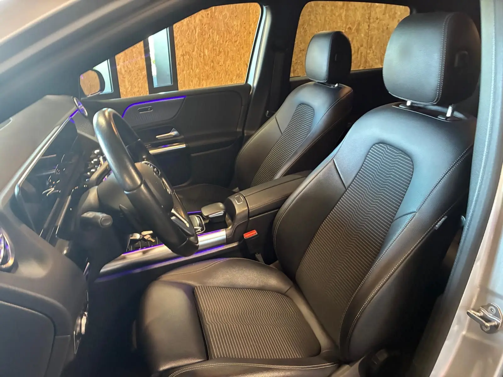 Vue intérieure côté conducteur de la Mercedes Classe B 200D gris, sièges en cuir noir avec éclairage d'ambiance violet.