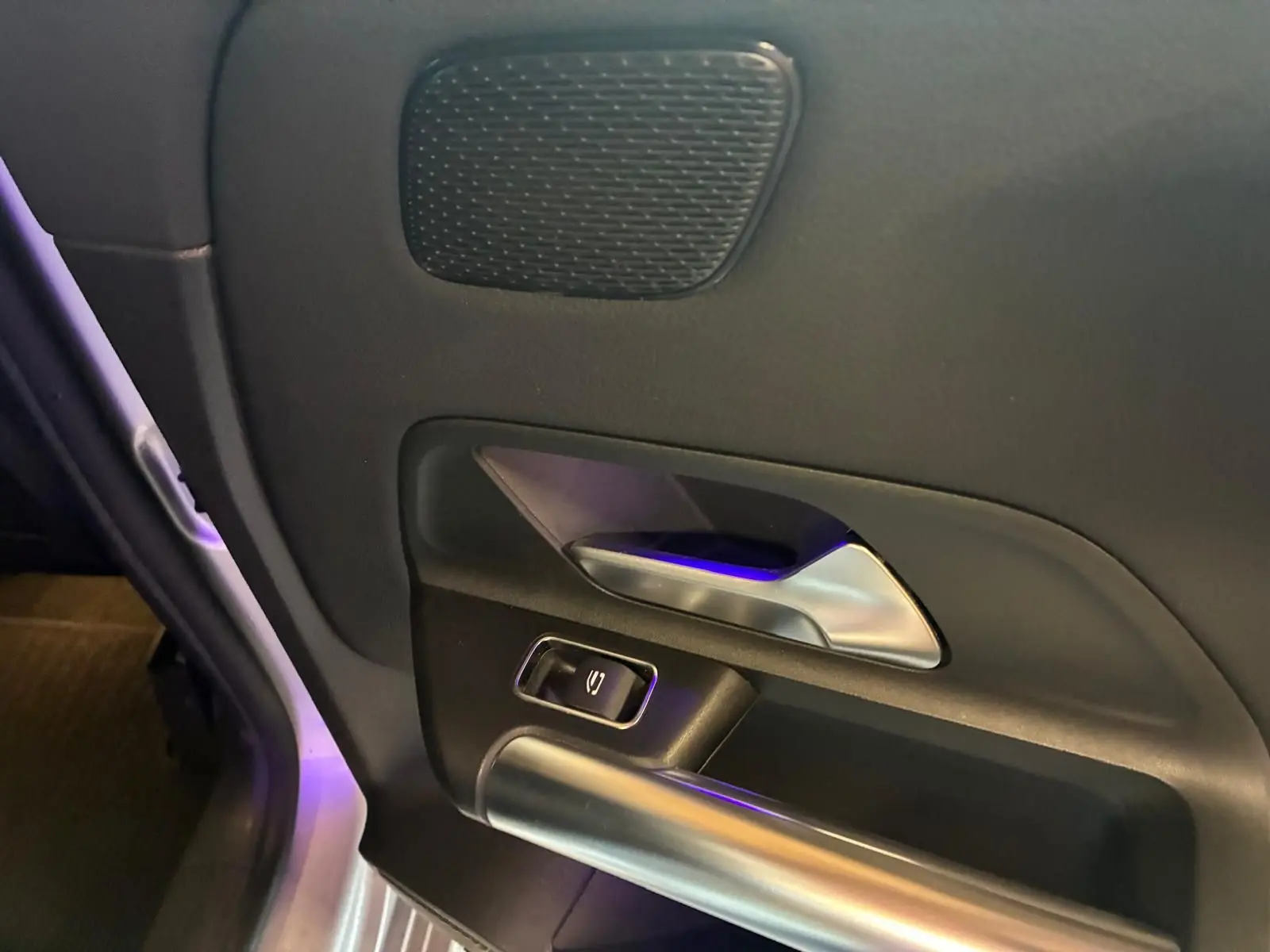 Gros plan sur la poignée intérieure côté gauche de la porte d’une Mercedes Classe B 200D gris, avec bouton de commande.