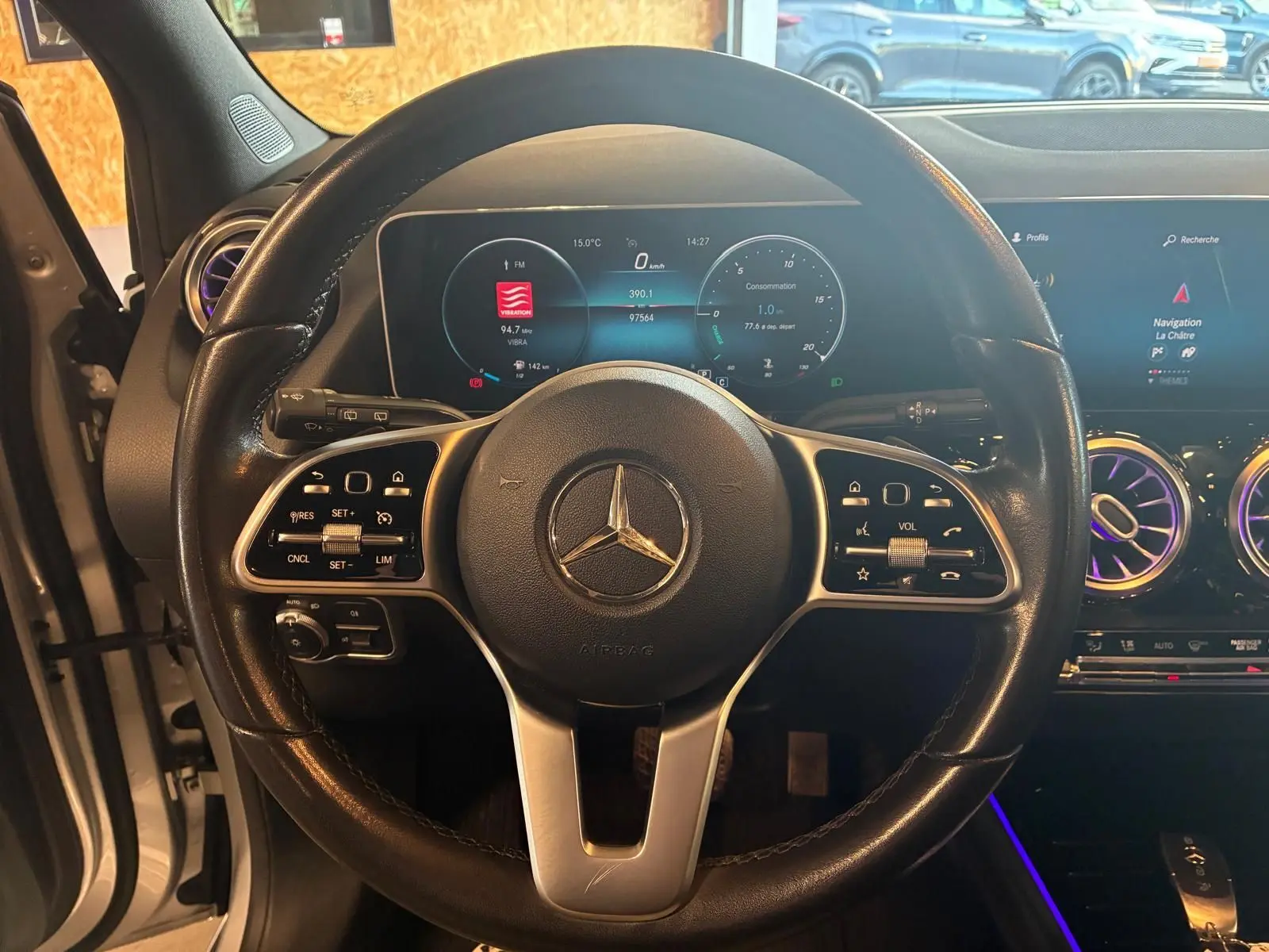 Vue intérieure centrée sur le volant cuir noir de la Mercedes Classe B 200D 2019 avec tableau de bord numérique et écran tactile.