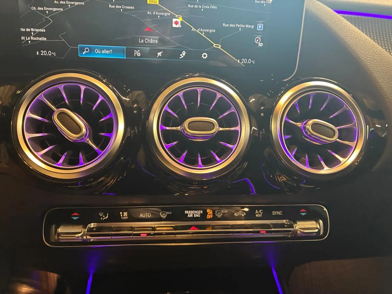Détail intérieur des aérateurs ronds illuminés en violet et de la console de climatisation d'une Mercedes Classe B 200D 2019 gris.