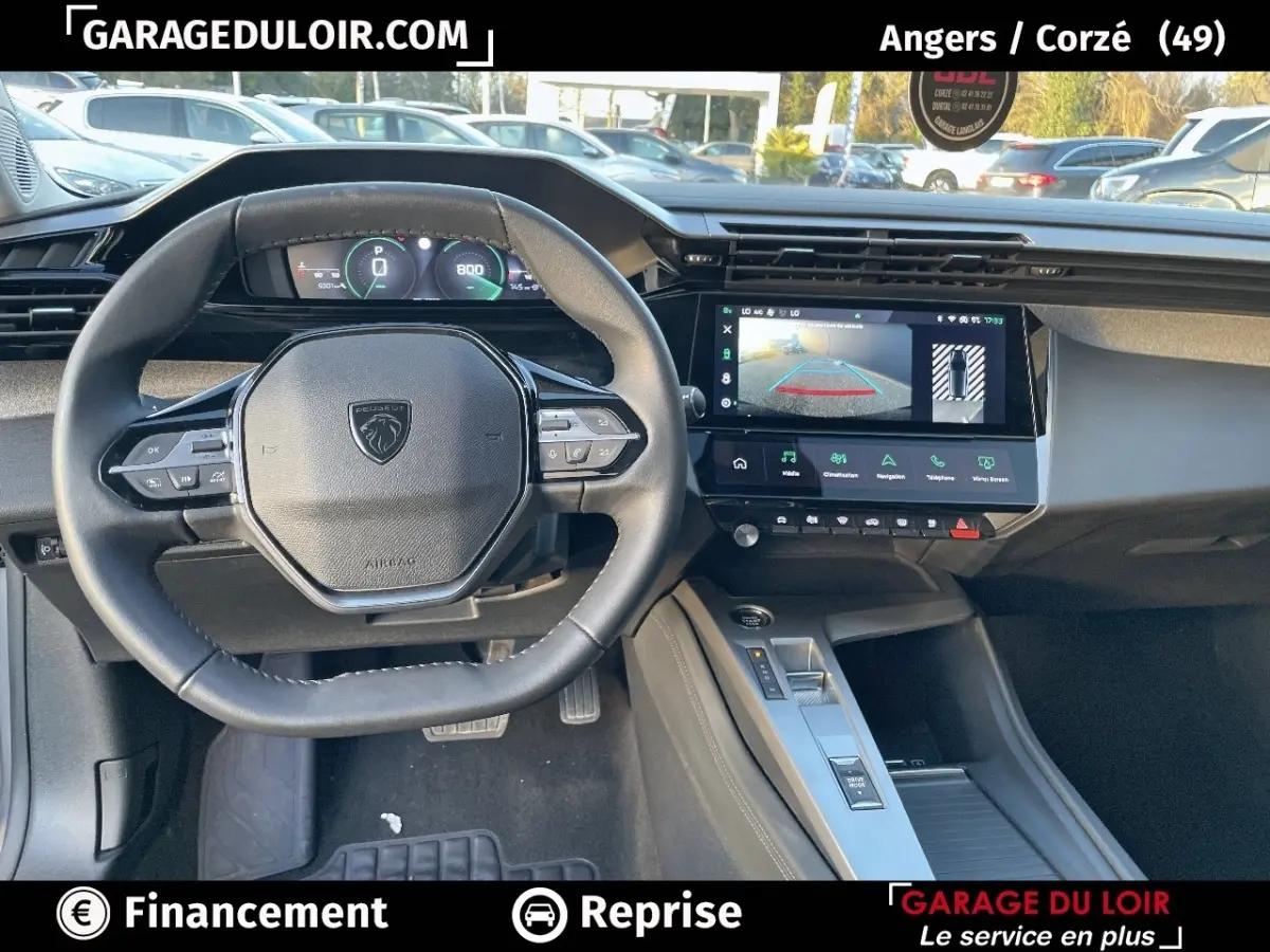 Vue intérieure du poste de conduite de la Peugeot 308 2024 gris foncé, avec volant compact et écran tactile central affichant la caméra de recul.