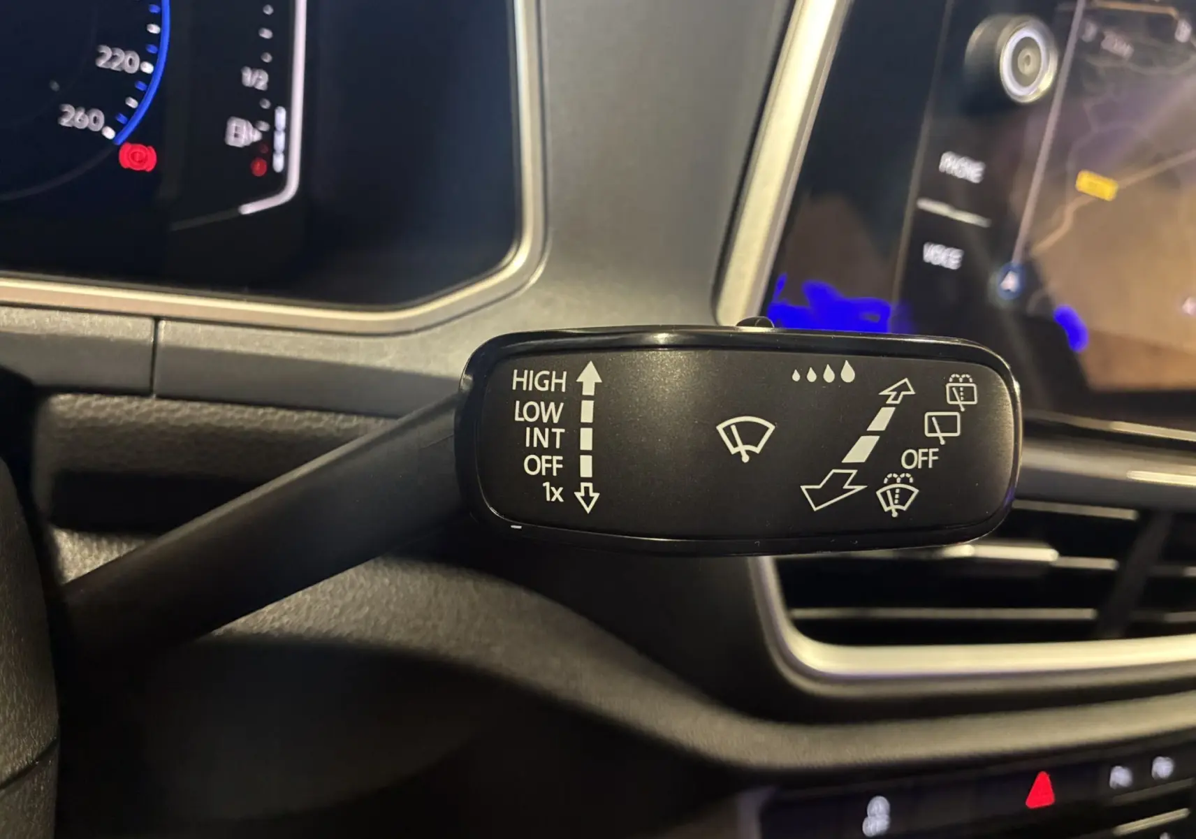 Gros plan sur la commande des essuie-glaces du Volkswagen T-Roc noir, tableau de bord et écran tactile en arrière-plan.