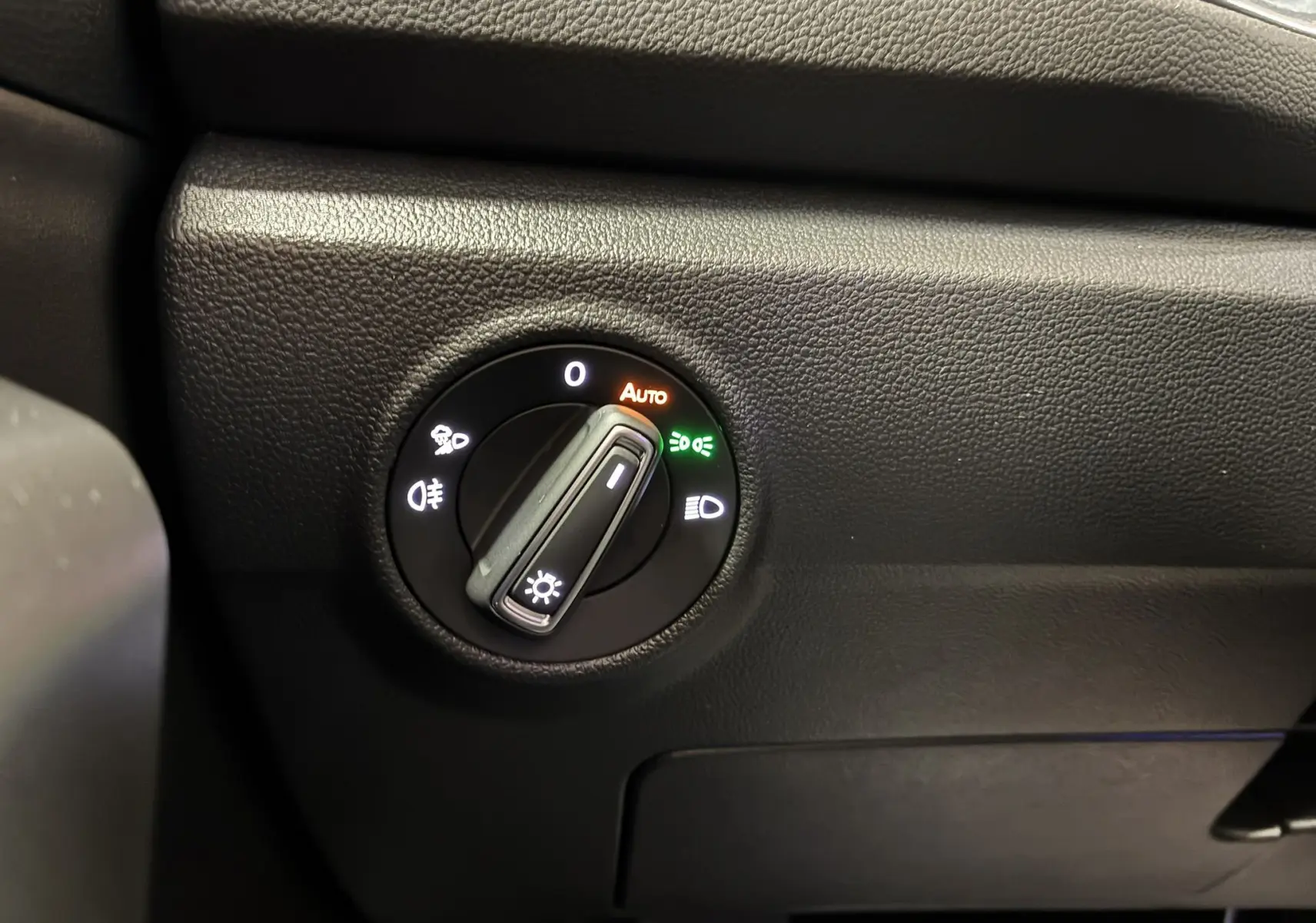 Gros plan sur le bouton de commande des phares du Volkswagen T-Roc 2025, tableau de bord noir texturé.