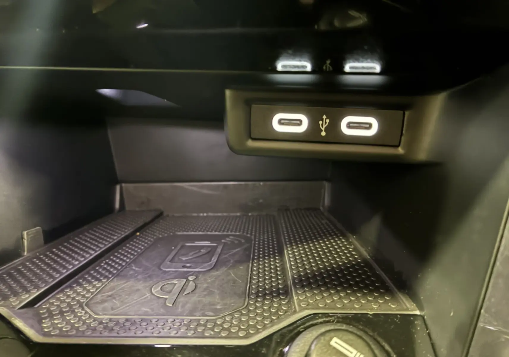 Gros plan sur la zone de recharge sans fil et les deux ports USB-C éclairés du Volkswagen T-Roc noir 2025.