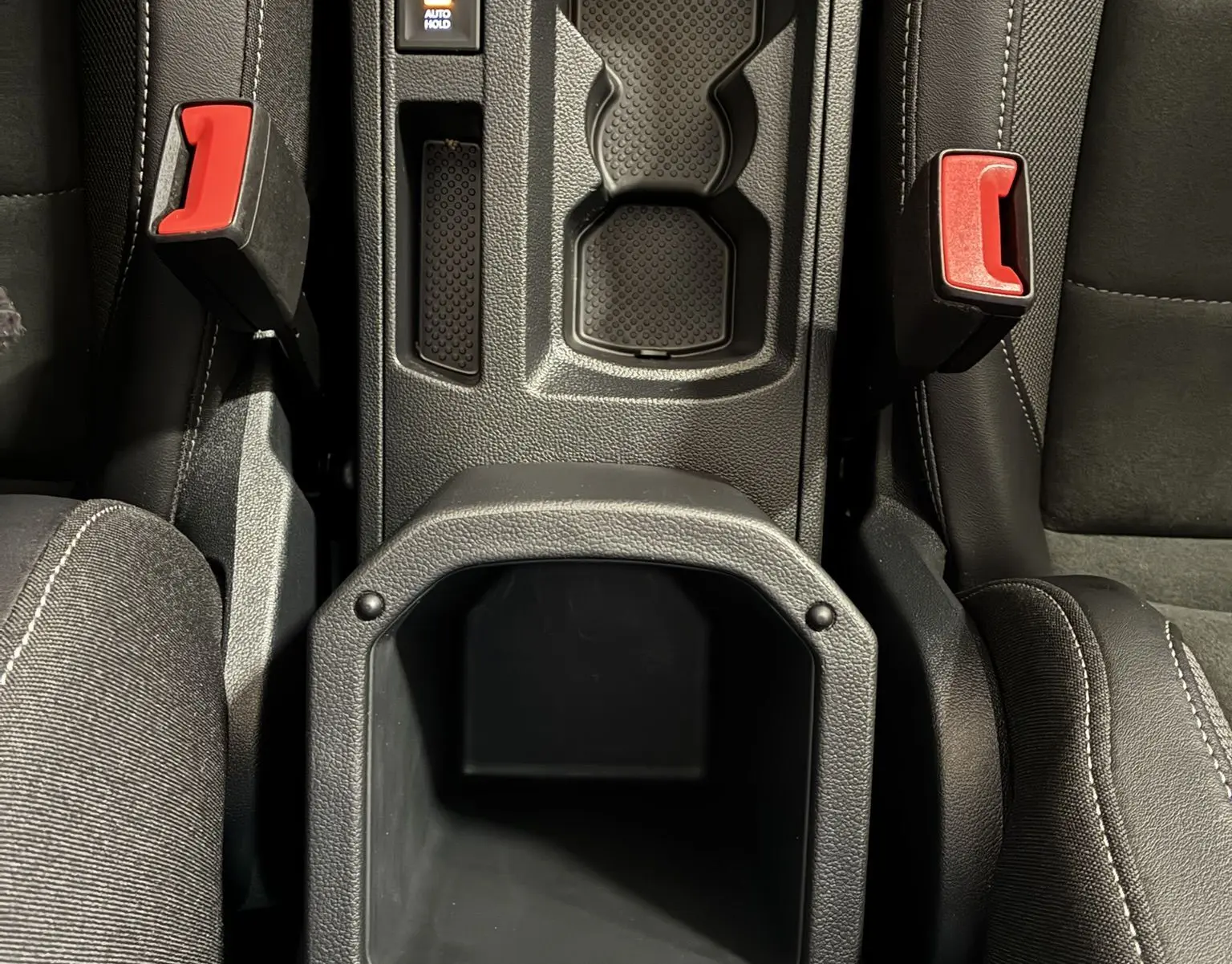 Vue plongeante sur la console centrale noire du Volkswagen T-Roc 2025, avec porte-gobelets et boutons électroniques visibles.