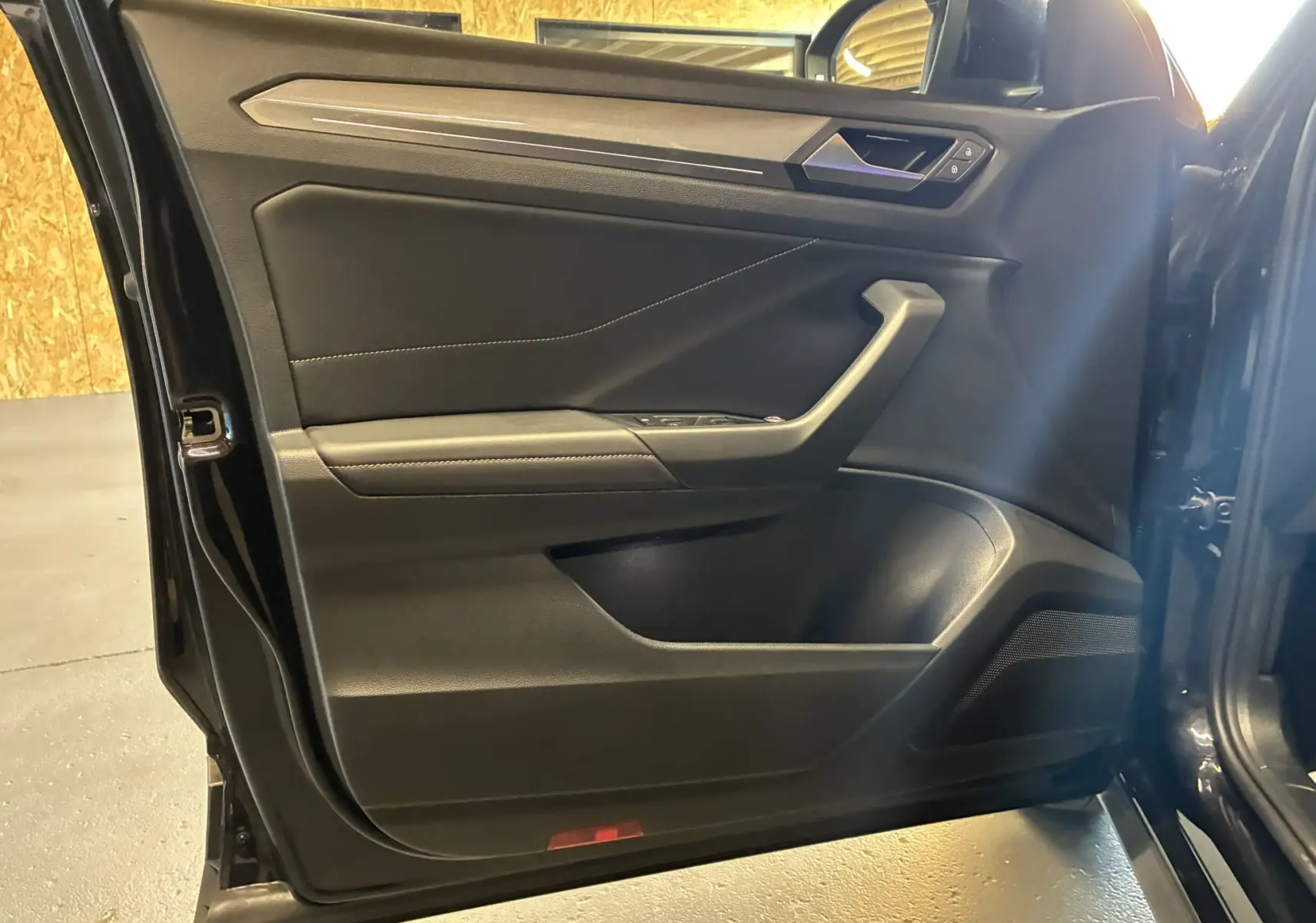 Vue intérieure de la porte avant gauche noire du Volkswagen T-Roc 2025 avec garniture tissu et détails en plastique.
