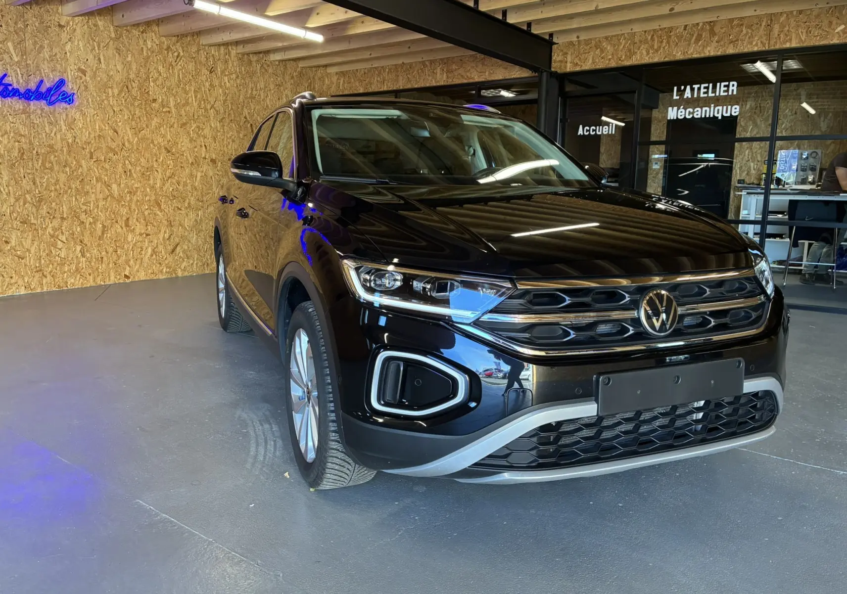 Volkswagen T-Roc noir 2025 en 3/4 avant droit, avec calandre chromée et phares LED, stationné en intérieur.