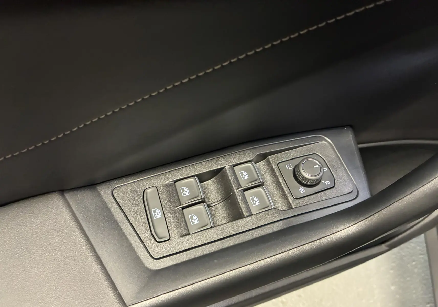 Vue rapprochée des commandes des vitres et réglages des rétroviseurs sur la porte côté gauche d’un Volkswagen T-Roc noir.
