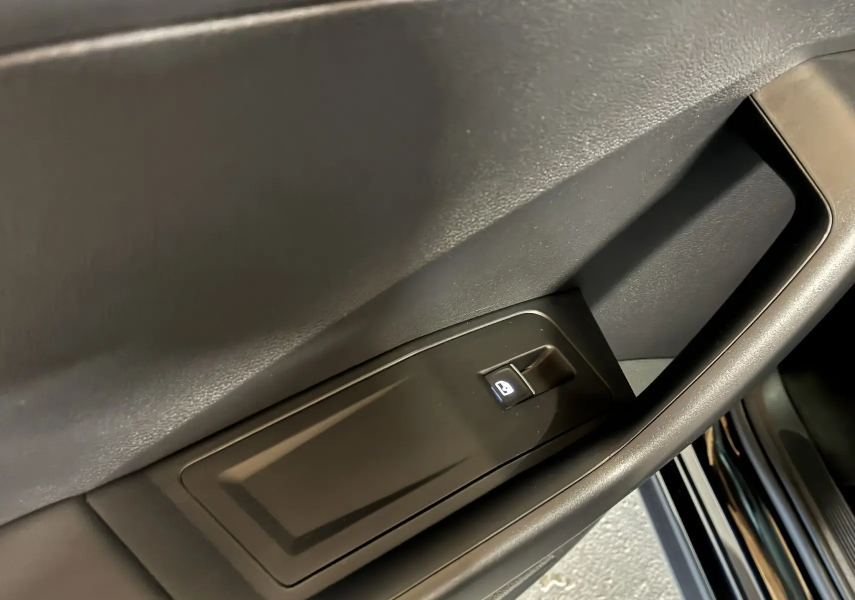 Gros plan sur la commande de lève-vitre électrique côté gauche d'une Volkswagen T-Roc noire, intérieur tissu noir.