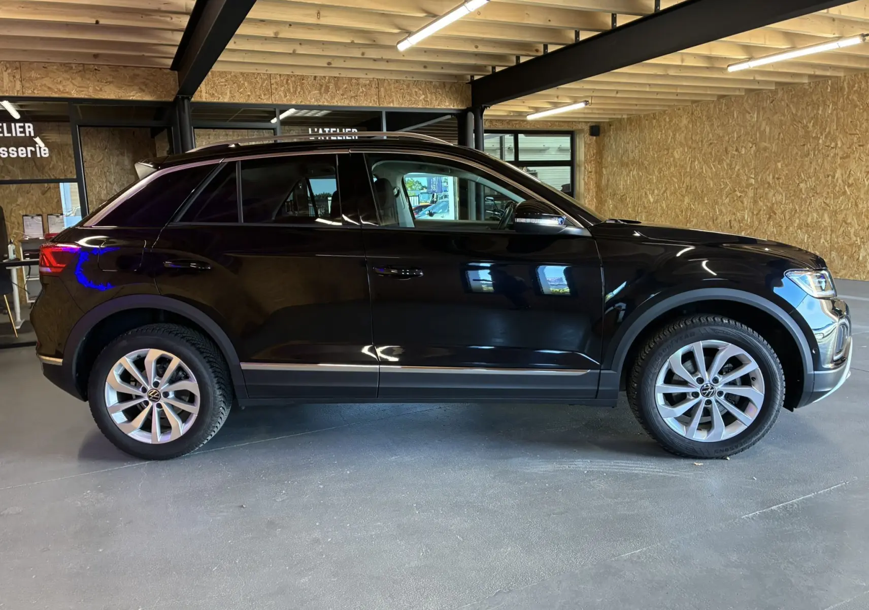 Vue de profil côté gauche d'un Volkswagen T-Roc noir 2025 garé en intérieur avec jantes alliage visibles.
