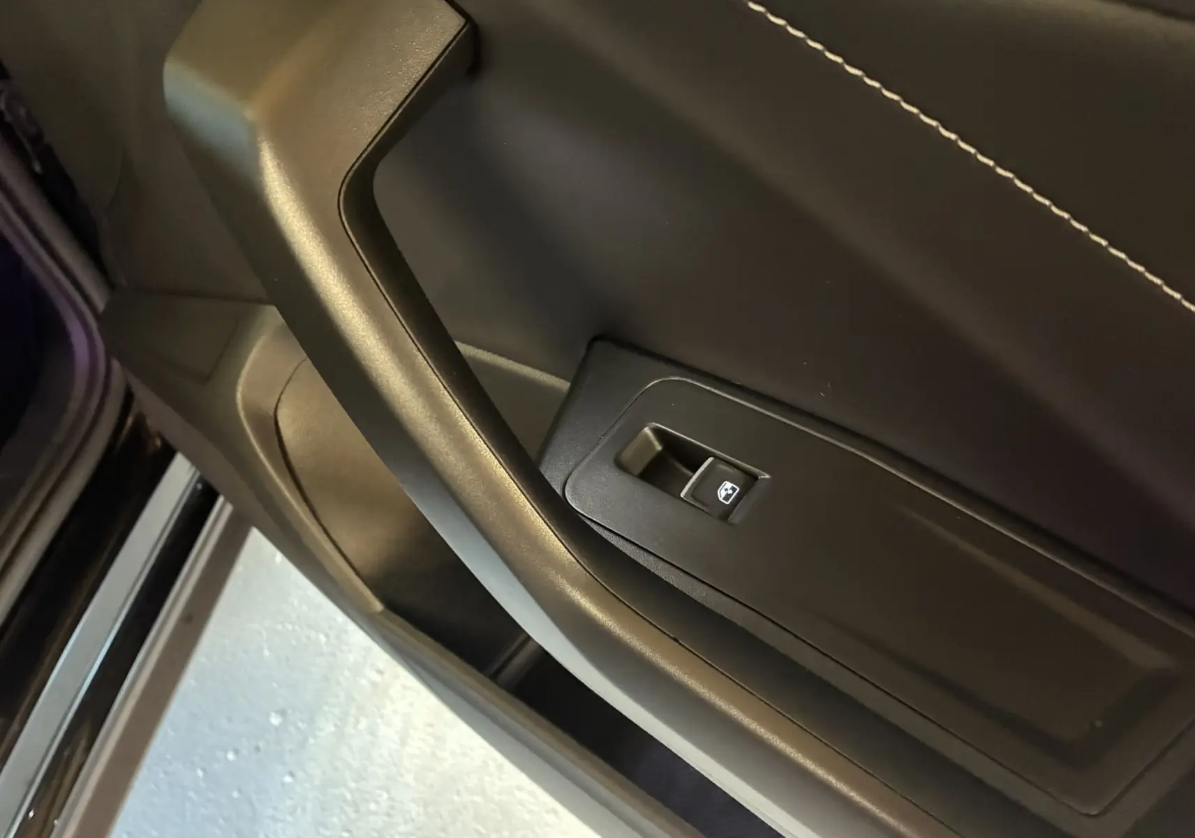 Détail de la commande de lève-vitre côté gauche en plastique noir avec surpiqûres blanches sur la porte intérieure du Volkswagen T-Roc noir.