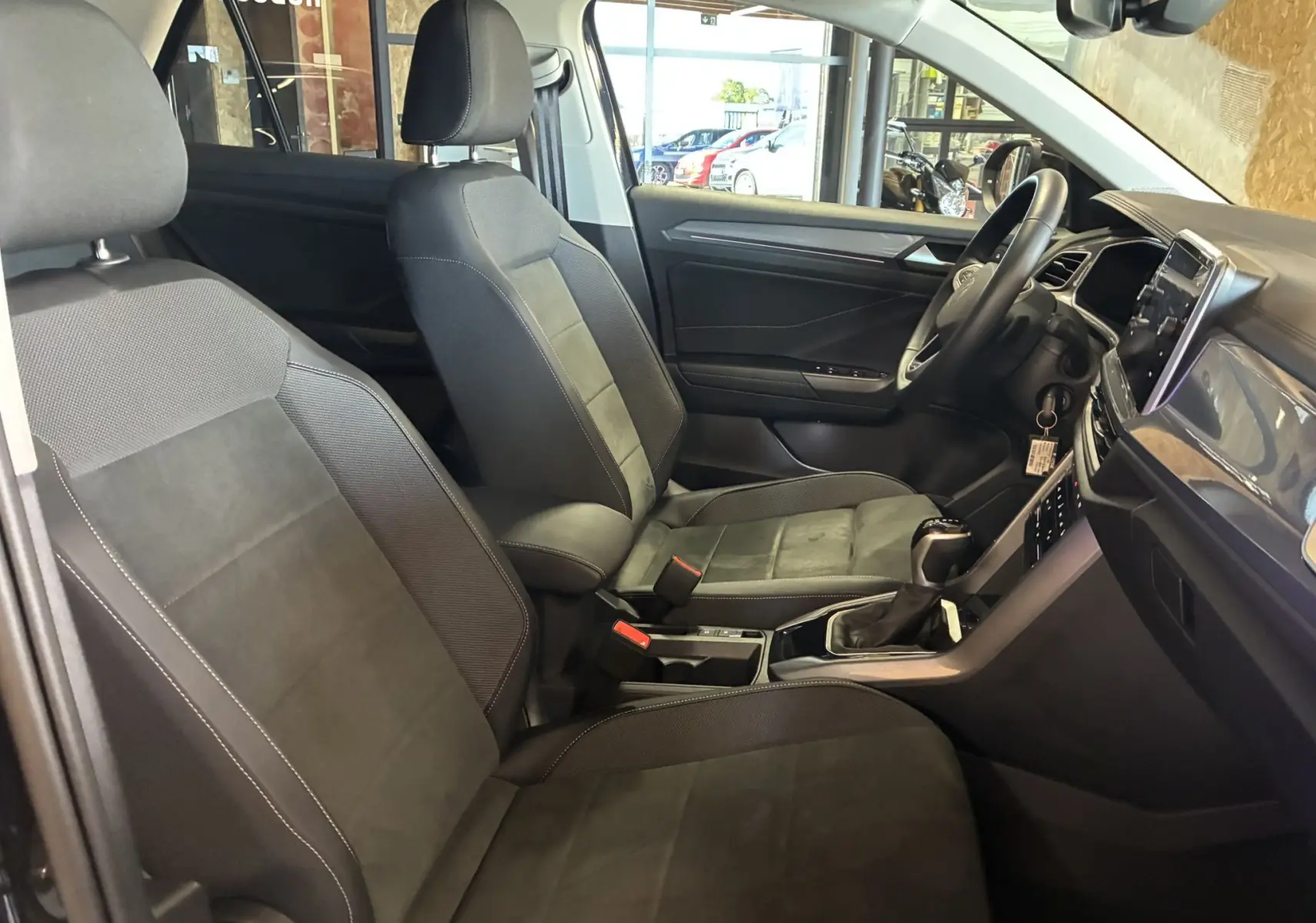 Vue intérieure côté gauche du Volkswagen T-Roc 2025, montrant les sièges en tissu noir et le tableau de bord moderne.