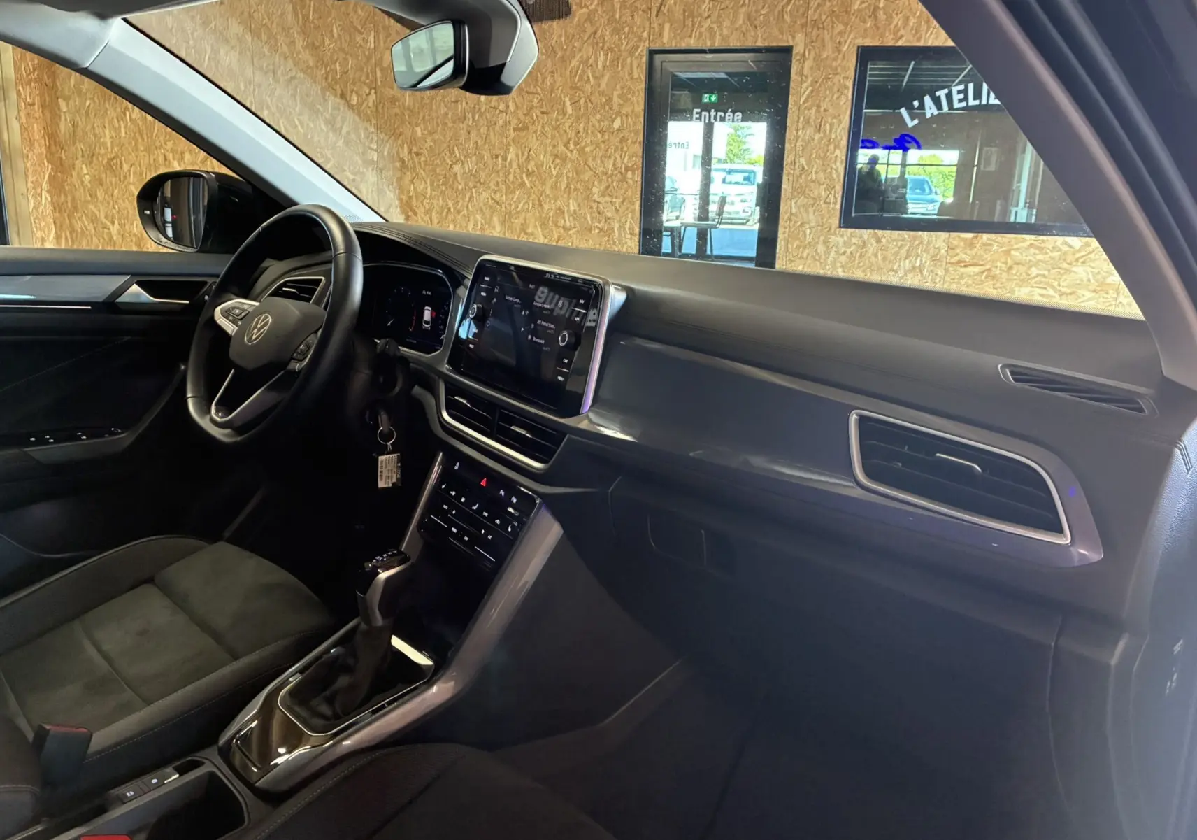 Vue intérieure côté conducteur du Volkswagen T-Roc 2025 noir, mettant en valeur le tableau de bord moderne et l’écran tactile central.