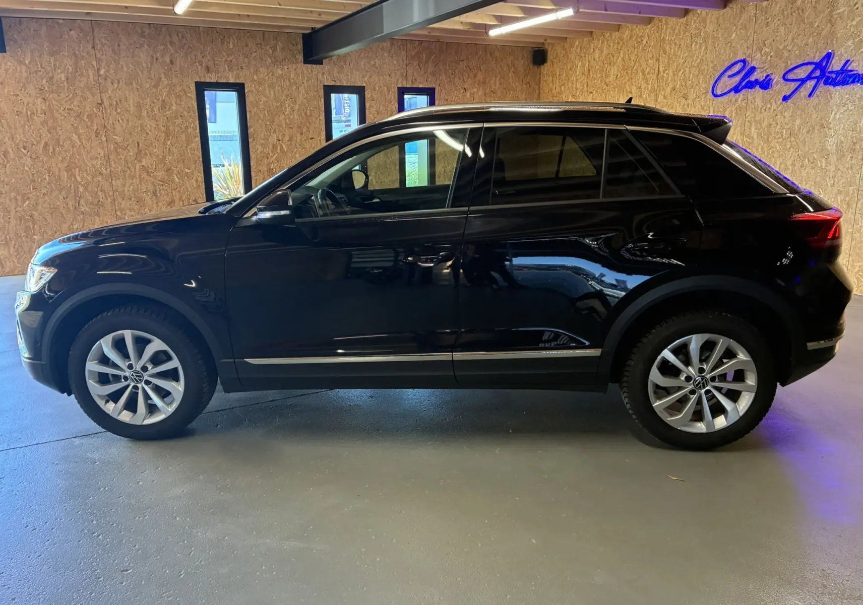 Vue de profil côté gauche d’un Volkswagen T-Roc noir 2025 garé en intérieur avec jantes alliage et toit noir.