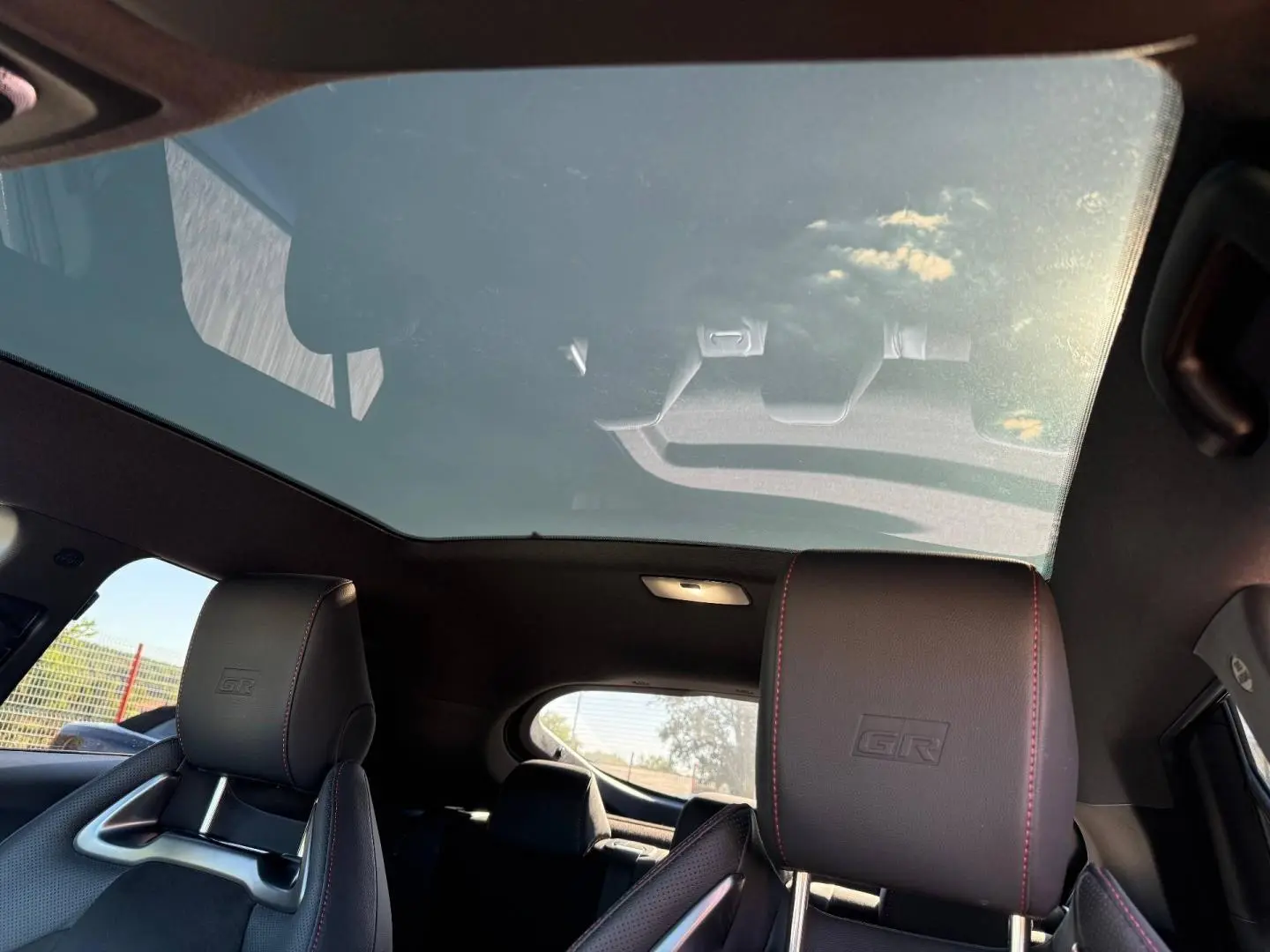 Vue intérieure arrière du Toyota C-HR 2.0 Hybride GR Sport avec toit panoramique et sièges sport noirs à surpiqûres rouges.