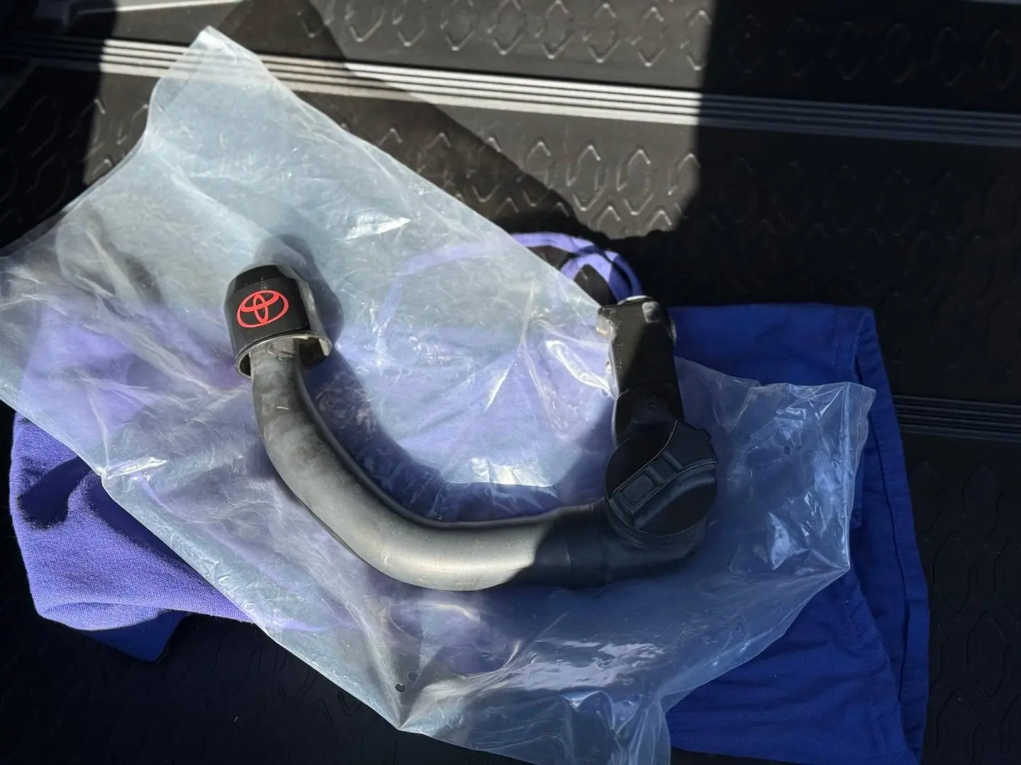 Gros plan sur un attelage de remorque noir avec logo Toyota rouge, posé sur un tissu bleu dans un coffre.
