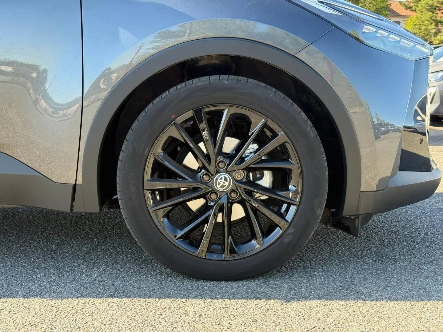 Gros plan sur la roue avant droite avec jante alu noire du Toyota C-HR gris Atlas métallisé bi-ton.