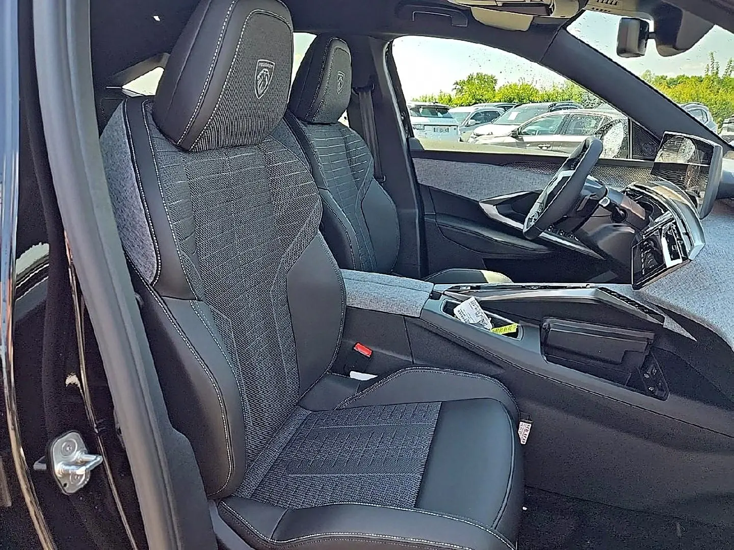 Vue intérieure côté gauche du Peugeot 3008 noir 2026, sièges tissu et cuir avec logo Peugeot brodé sur appuie-tête.